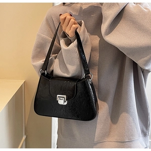 Close-up of black glossy underarm bag with silver buckle and textured patent leather