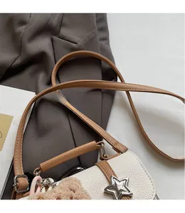 Detail of white lychee leather bag with star-shaped metal lock and brown plush bear charm