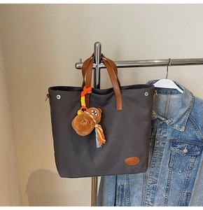 Close-up of grey canvas tote with leather handles and a plush bear charm on a denim background