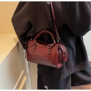 Detailansicht einer weinroten Boston-Tasche aus Lackleder mit Nieten und Doppelgriffen