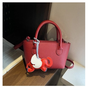 Red lychee pattern leather bucket bag with an elephant charm on a wooden table