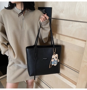 Detail of black pebbled leather tote bag with long handles and teddy bear pendant