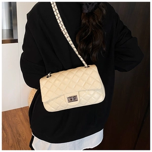 Close-up of quilted cream crossbody bag with metal chain strap and rotating clasp detail