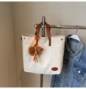 Detail view of canvas tote bag featuring brown leather handle and cute plush bear charm