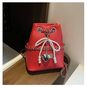 Detail of red bucket bag with litchi texture, pearl bow and silver heart pendant charm