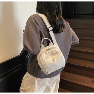 Close-up of off-white nylon shell bag with metal logo and green side label on wooden stairs