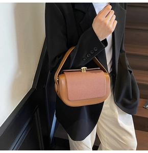 Detail of camel brown leather handbag showing textured flap and gold buckle on a model