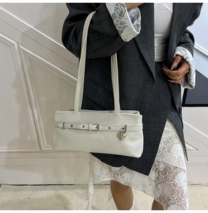 Detail of cream white faux leather shoulder bag with silver eyelets and heart pendant