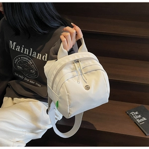 Detail of white nylon shell bag with metal logo and front zipper on model's shoulder