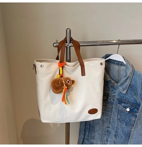 Detail of cream canvas tote bag with brown leather handles and plush bear charm