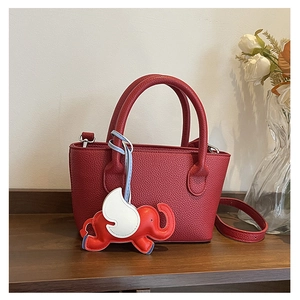 Detail shot of red pebbled leather tote bag with a cute elephant pendant on a wooden base