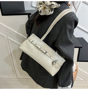 Detail view of pearl white underarm bag with decorative belt strap and heart pendant