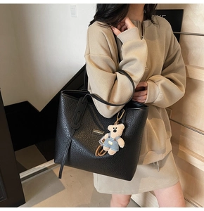 Detail of black pebbled leather tote bag with long straps and a cute plush bear charm