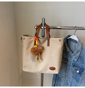 Detail of beige canvas tote bag with brown handles and a cute plush bear charm