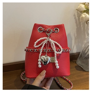 Detail of red lychee leather mini bucket bag with pearl bow and silver heart pendant