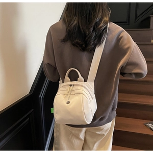 Rear view of a model wearing a multi-pocket cream canvas shell bag with wide shoulder straps