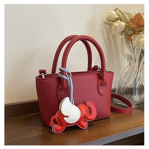Detailed view of mini red leather bucket bag with a decorative elephant charm on wood