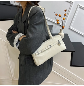 Detail of cream glossy leather shoulder bag featuring silver heart pendant and buckle strap
