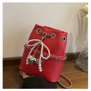 Macro shot of red bucket bag showing pebbled leather texture and pearl bow detail