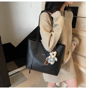 Detail of black lychee grain leather tote bag featuring a cute teddy bear charm hanging