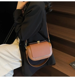Close-up of caramel leather crossbody bag featuring gold twist lock and textured fabric flap