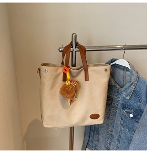 Detail of canvas tote bag with brown leather handles and cute plush bear charm