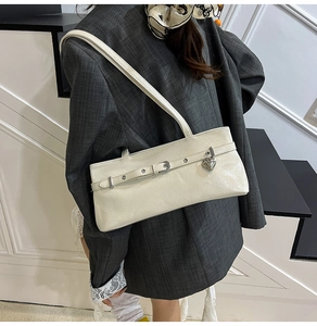 Close-up of minimalist cream underarm bag with silver heart pendant and metal strap detail