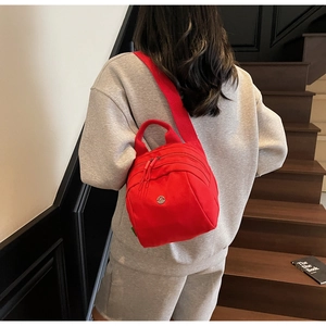 Detail of red canvas crossbody shell bag with metal M logo and multiple zipper compartments