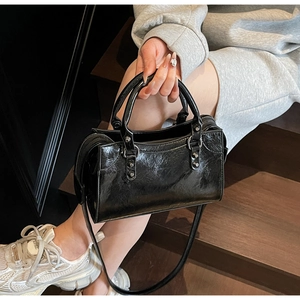 Detail einer schwarzen Lackleder-Handtasche mit silbernen Nieten und Beschlägen auf Holzstufen