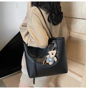 Detail of black pebbled leather tote bag with blue bear charm in modern interior