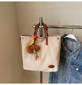 Close-up of canvas tote bag featuring brown leather logo patch and cute bear plush charm