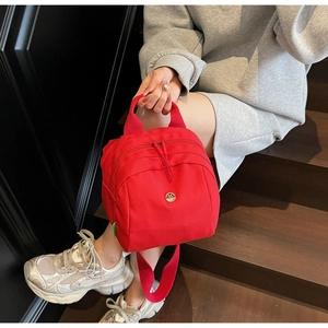 Detail of red nylon handbag featuring double zipper and metallic M logo on steps