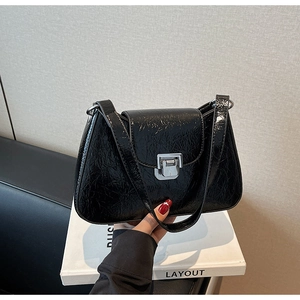 Detail of glossy wrinkled black leather underarm bag featuring a silver metal buckle closure