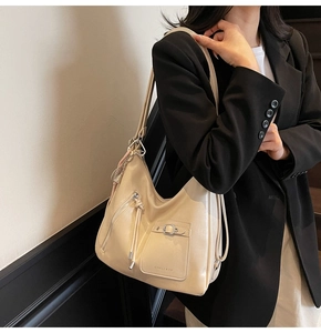Close-up of beige tote bag with silver square buckle, decorative zipper and tassels