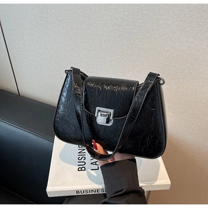 Close-up of black glossy crinkled leather underarm bag with a silver square clasp
