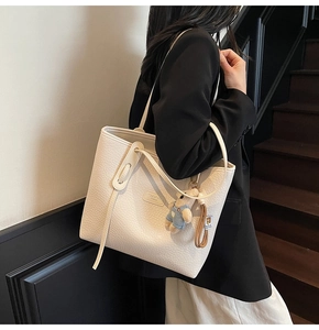 Detailed side view of cream white lychee leather tote bag with cute bear charm
