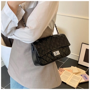 Detail of a black quilted leather crossbody bag with metal chain strap and turn-lock closure