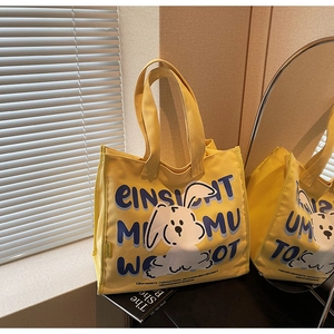 Detailed view of yellow canvas tote bag featuring cute cartoon rabbit and blue artistic text