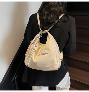Close-up of cream soft leather tote bag featuring a decorative metal buckle and tassel detail