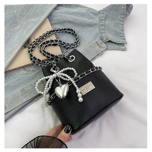 Detail of black lychee texture bucket bag with silver chain and pearl bow charm