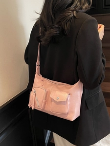 Pink faux leather shoulder bag with functional front pockets on a model in a black suit