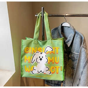 Detail view of green canvas tote bag featuring white cartoon rabbit and bold yellow lettering