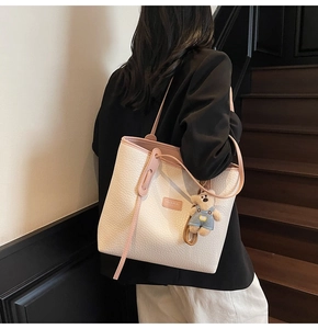 Detail of beige lychee pattern tote bag with pink trim and cute teddy bear charm accessory