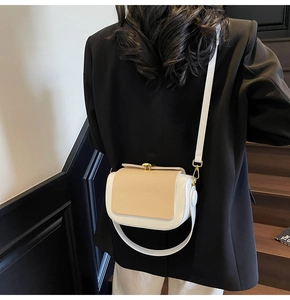 Detail of a chic cream and white contrast handbag with golden rotary lock on model