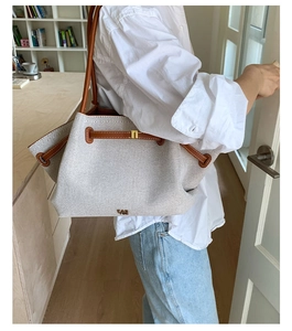 Detail of large tote bag featuring cream canvas and brown leather trim on model
