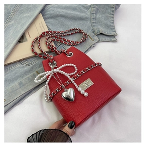 Detail of red leather bucket bag with pearl bow and silver heart pendant on denim