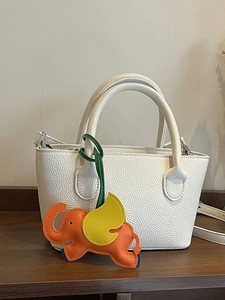 White lychee pattern leather bucket bag with a colorful elephant charm and crossbody strap