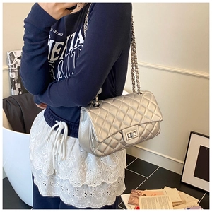 Detail of silver quilted flap bag with metal chain strap worn by a model in lifestyle setting