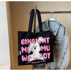 Detail of black canvas tote bag showing pink cartoon rabbit print and sturdy shoulder strap