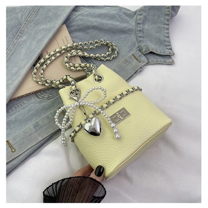 Detail of light yellow bucket bag with silver chain strap and pearl bow decoration